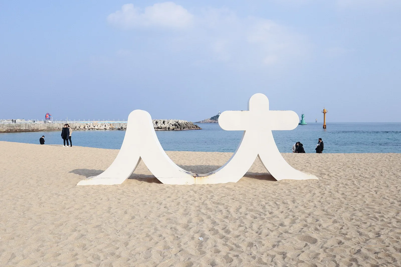 Uma escultura branca na areia da praia de Sokcho, com o mar e um quebra-mar por trás