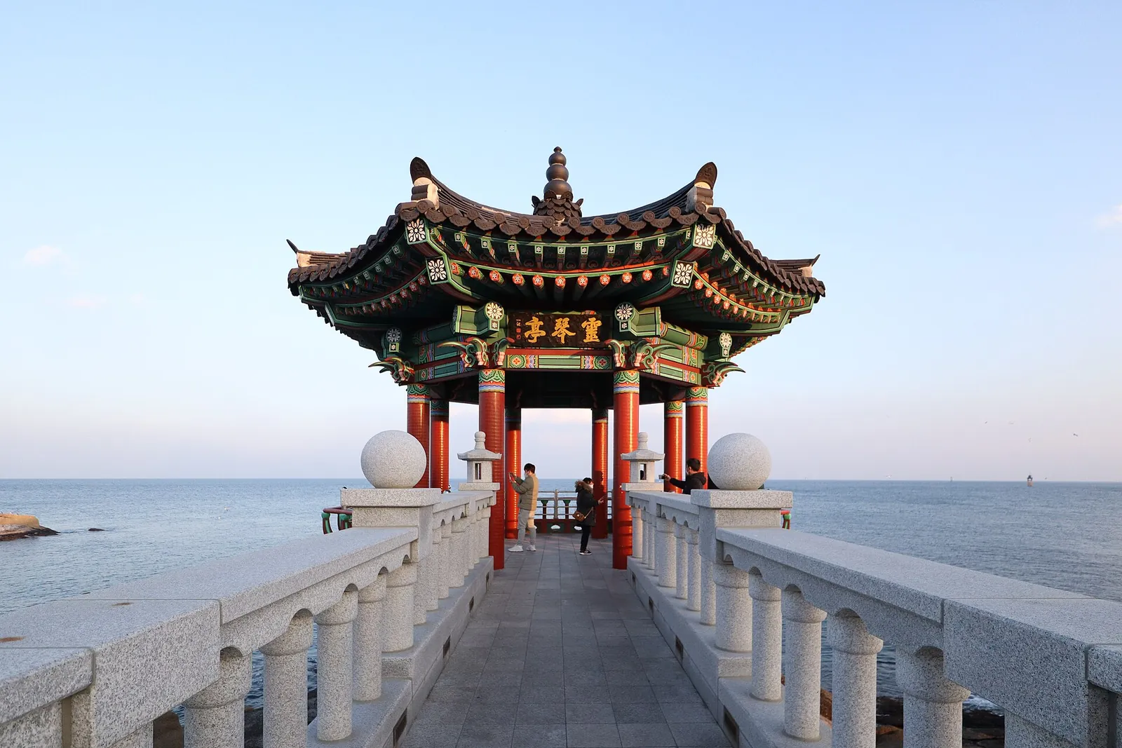 O pavilhão Yeonggeumjeong, de telhado de telha, no fim de uma ponte de balaustrada branca sobre o mar, em Sokcho