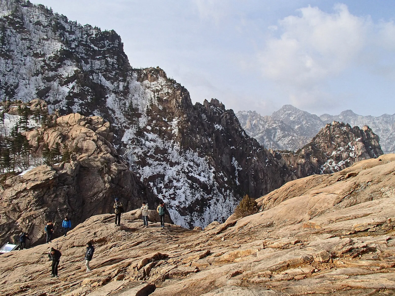 Visitantes a caminhar em rocha nua em Gwongeumseong, com picos de granito polvilhados de neve por trás