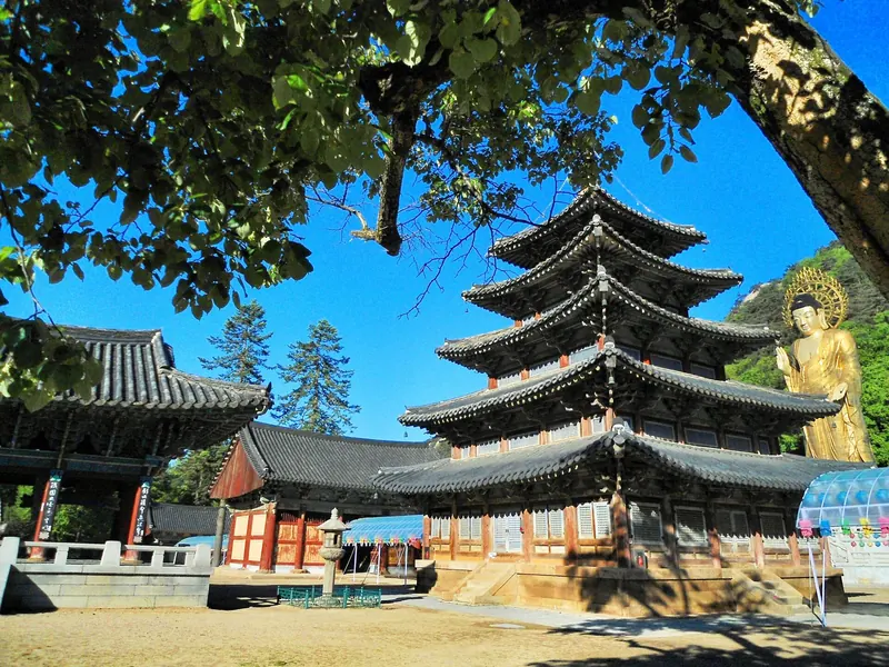 Palsangjeon, the five-storey wooden pagoda of Beopjusa, under a blue sky with the gilt Maitreya statue to the right