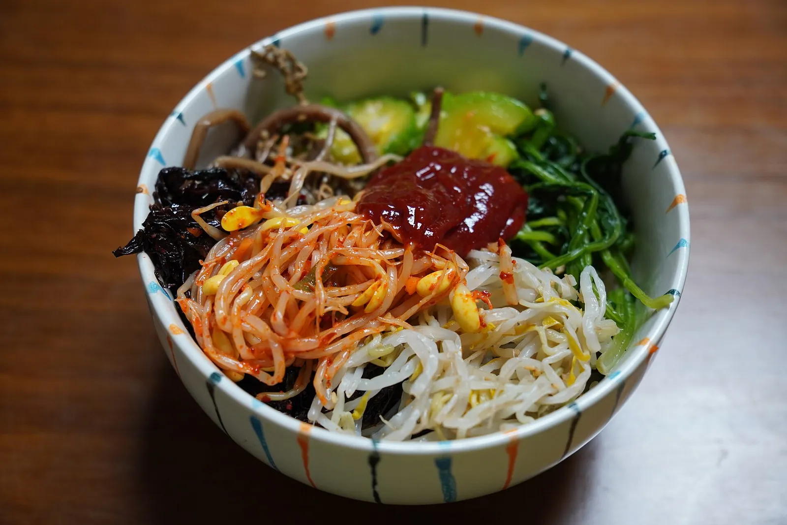 A bowl of sanchae bibimbap: rice topped with seasoned mountain greens, bean sprouts, shredded vegetables and red chilli paste