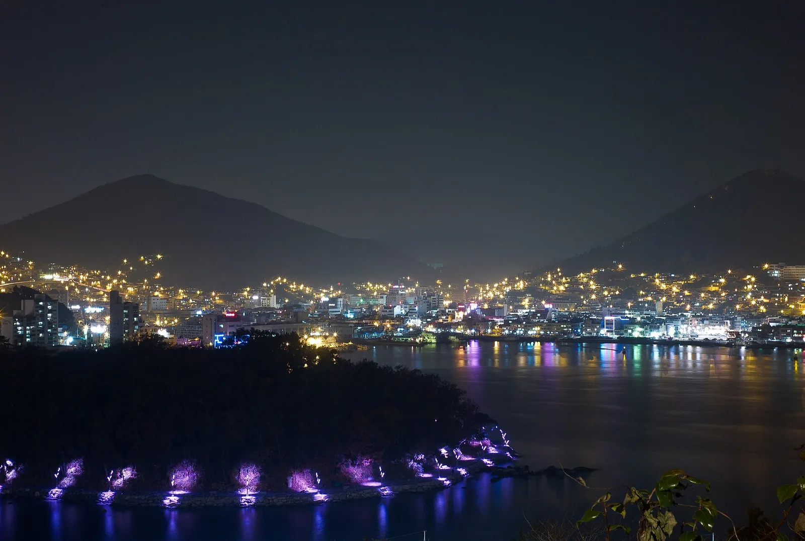 Yeosu harbour at night, with city lights reflected in the water below dark hills