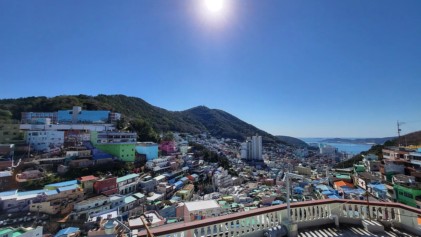 Colourful houses of Gamcheon Culture Village on a Busan hillside under a bright blue sky, with the sea beyond