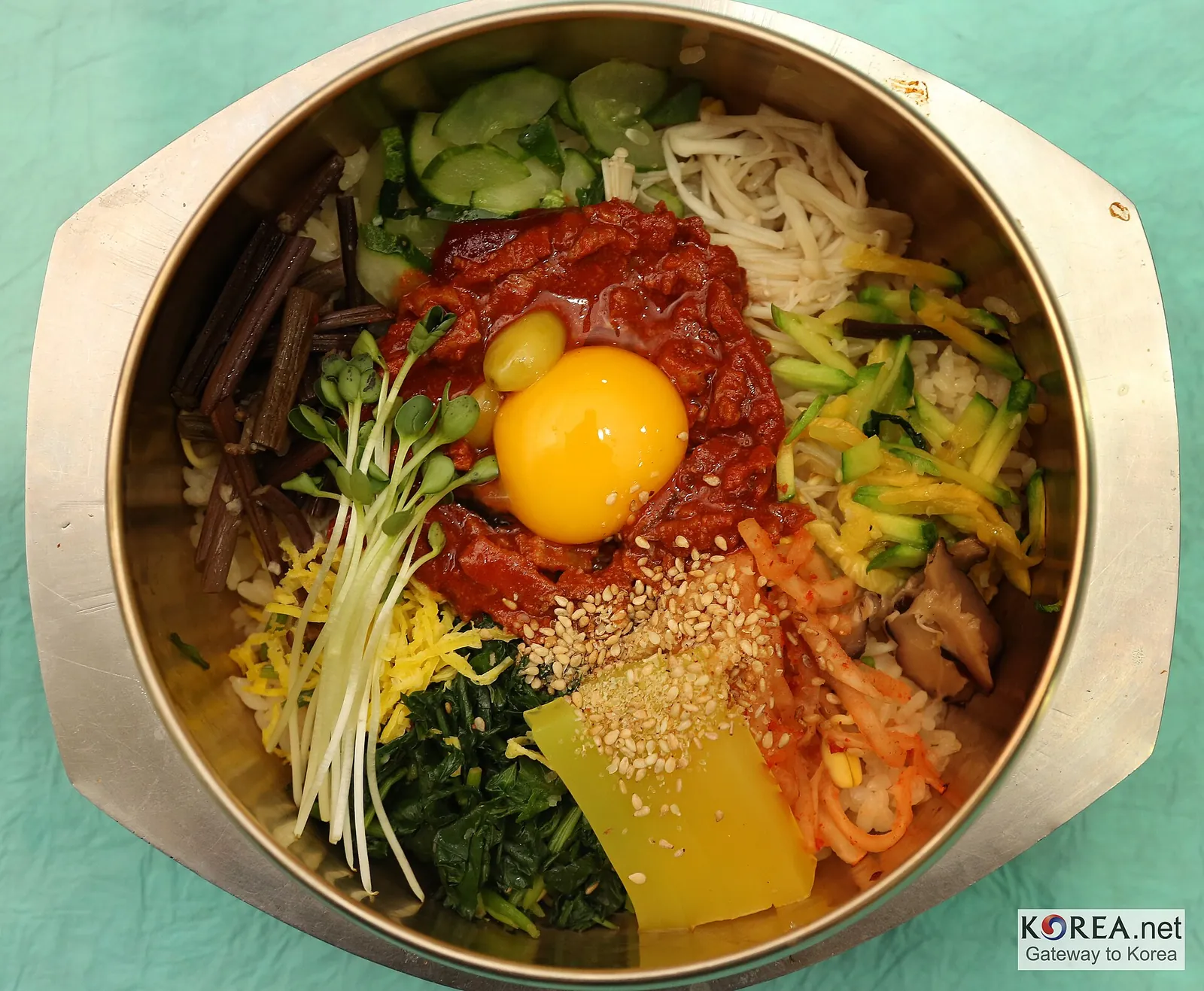 Bibimbap in a brass bowl: an egg yolk on red chilli paste, surrounded by bracken, spinach, bean sprouts, cucumber, mushrooms and a slice of yellow jelly
