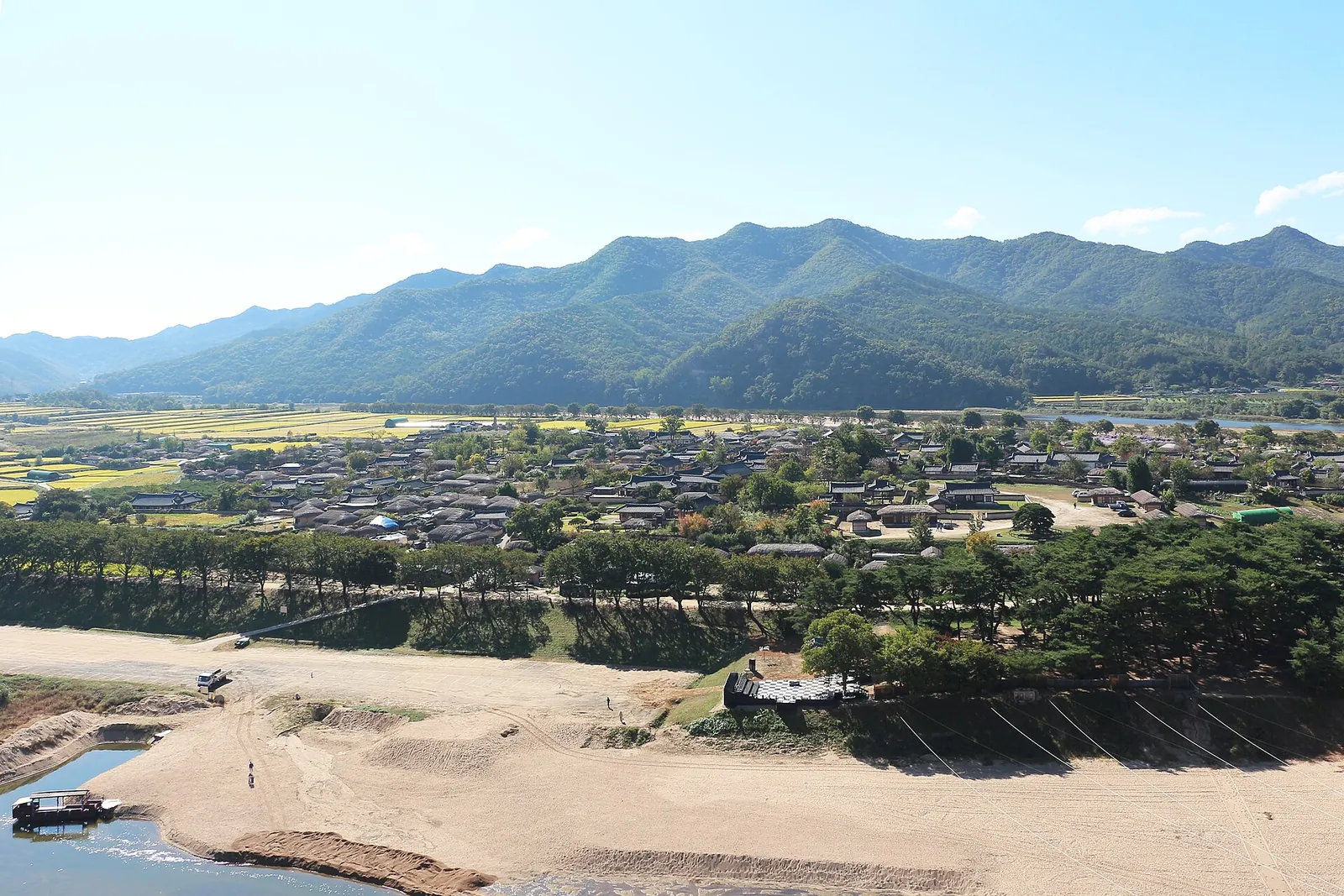 Hahoe Village's tiled and thatched roofs spread across a bend of the Nakdonggang River below a mountain ridge, with a sandy riverbank in front