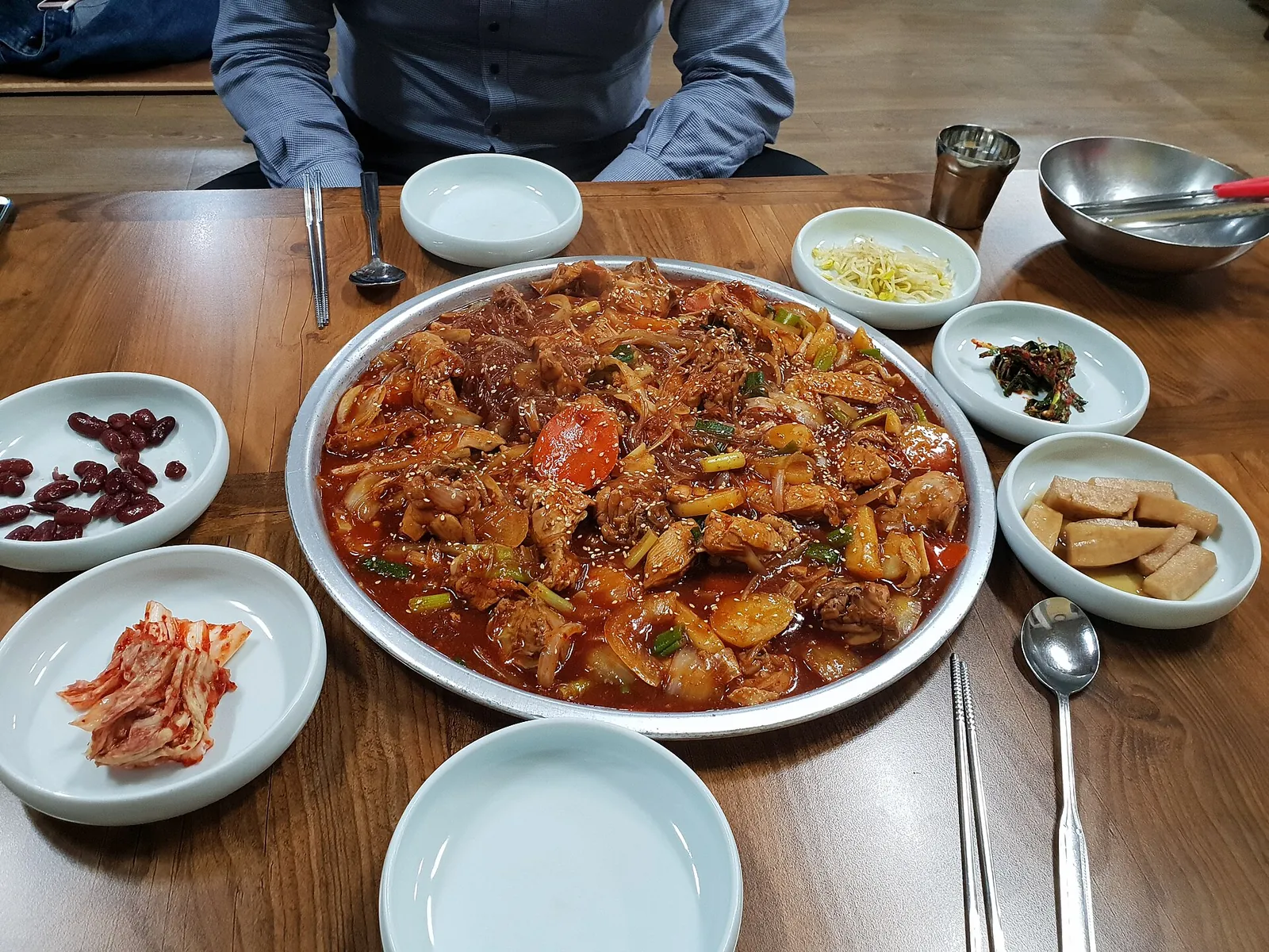 A large plate of Andong jjimdak, chicken braised with glass noodles and vegetables in a glossy red-brown sauce, with side dishes around it