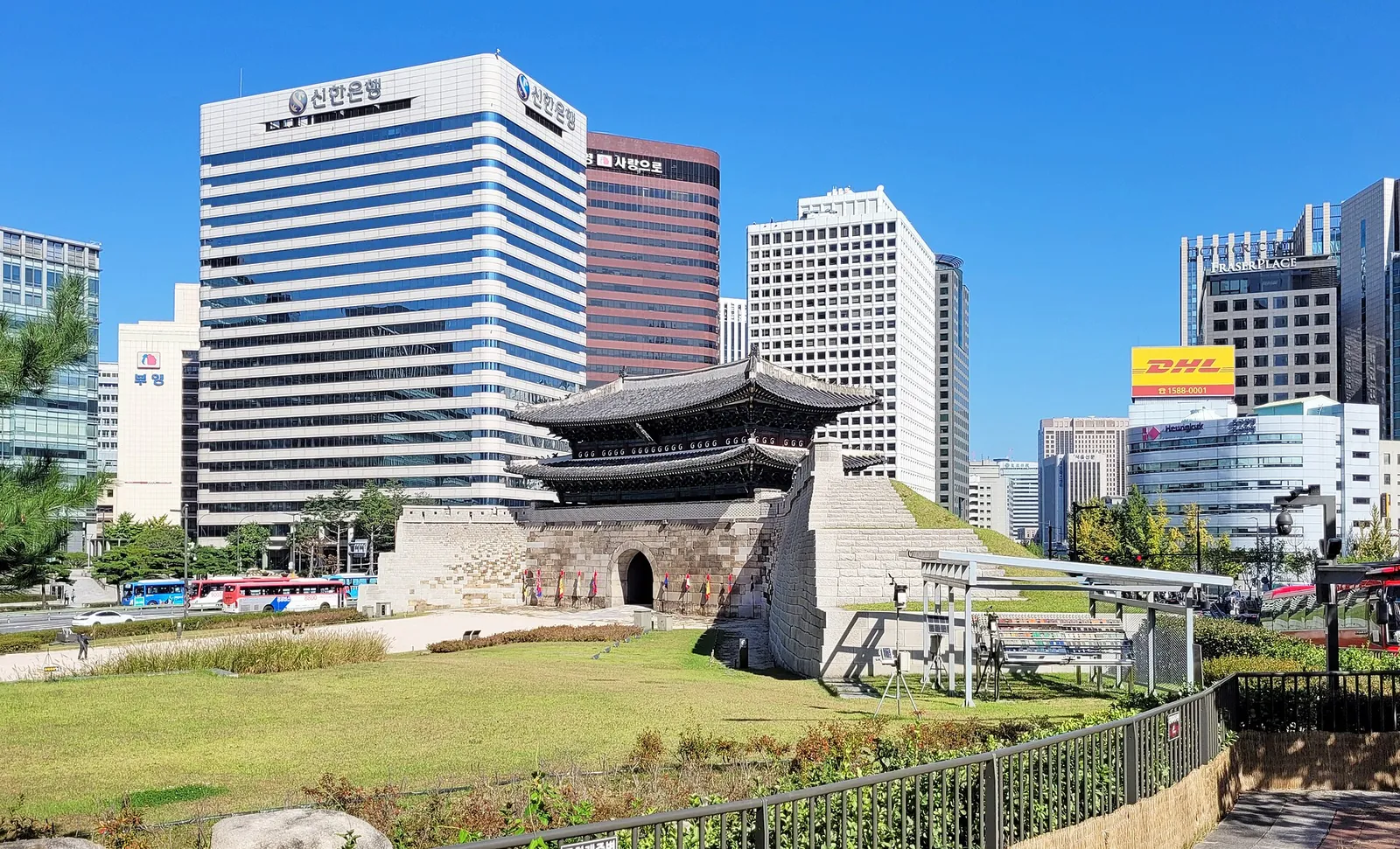 Sungnyemun, den historiske sydlige port i Seoul, med et tegltag i to etager over en stenbase og kontortårne bagved, under en blå himmel