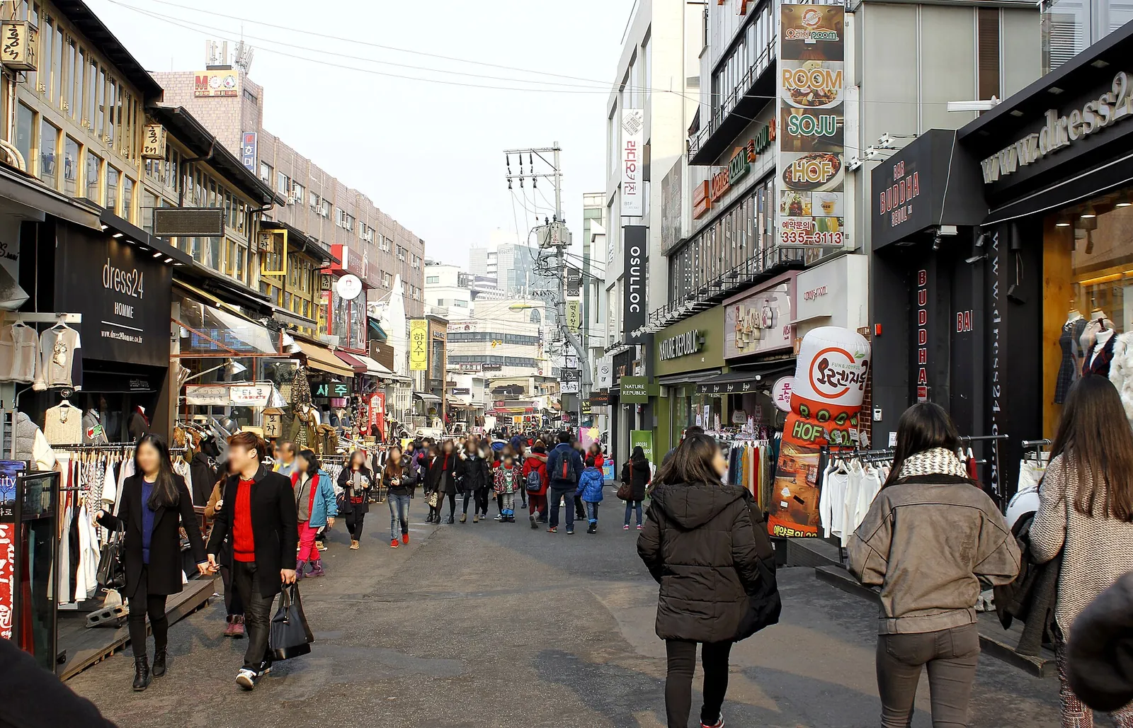 Fodgængere på en gade med butikker i Hongdae-kvarteret i Seoul i dagslys