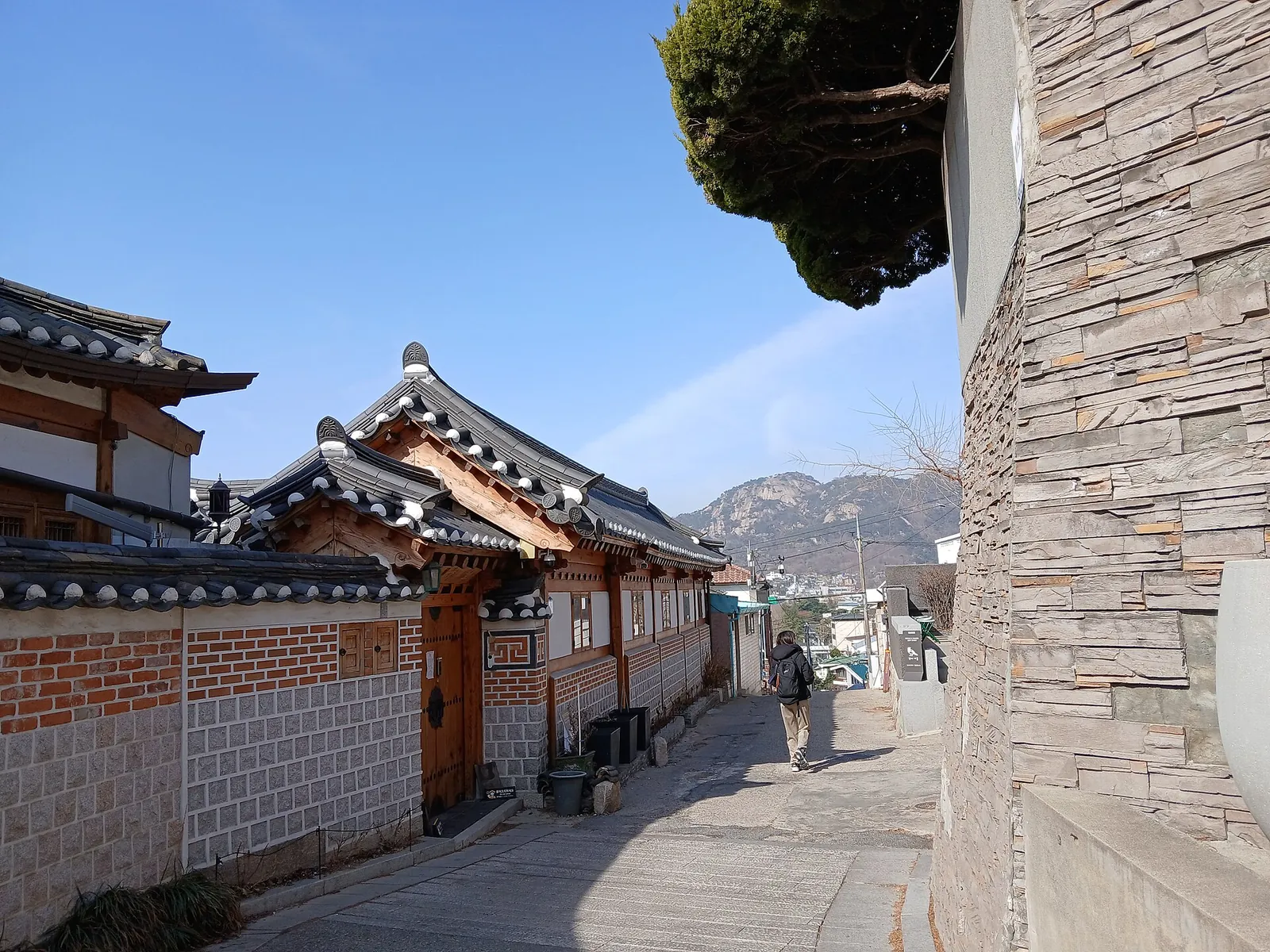 Hanok-tegltage og murstensmure i hanok-landsbyen Bukchon under en blå himmel, med en bakke bagved