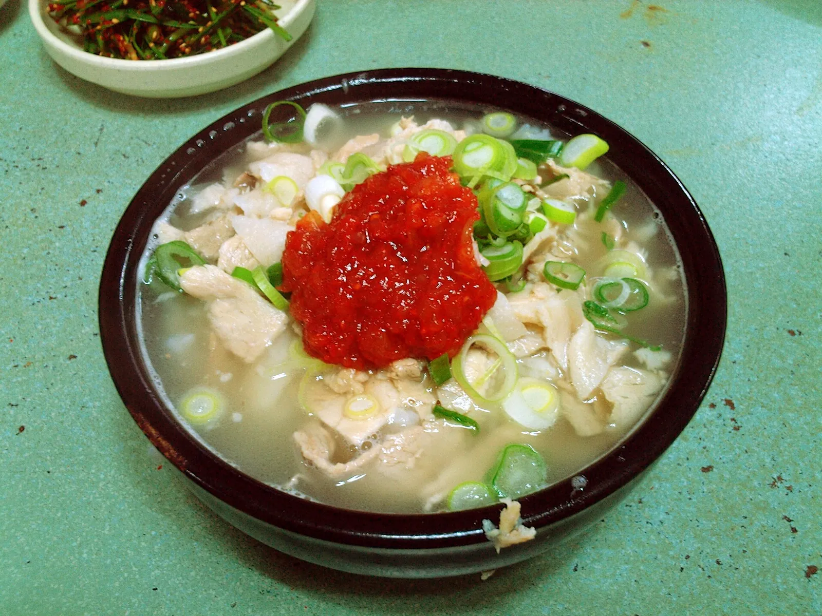 A bowl of dwaeji gukbap, pork and rice soup topped with spring onions and red chilli paste