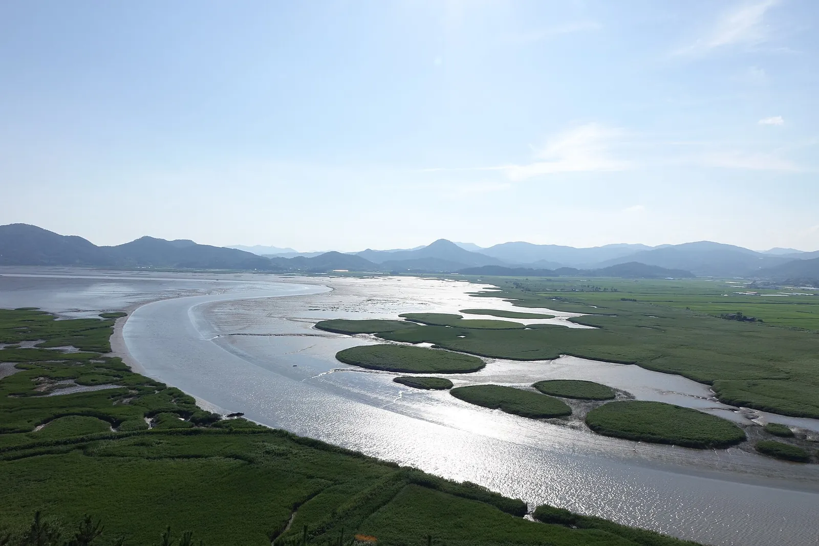The S-shaped tidal channel of Suncheon Bay winding through green reed beds and mudflats, with hills on the horizon