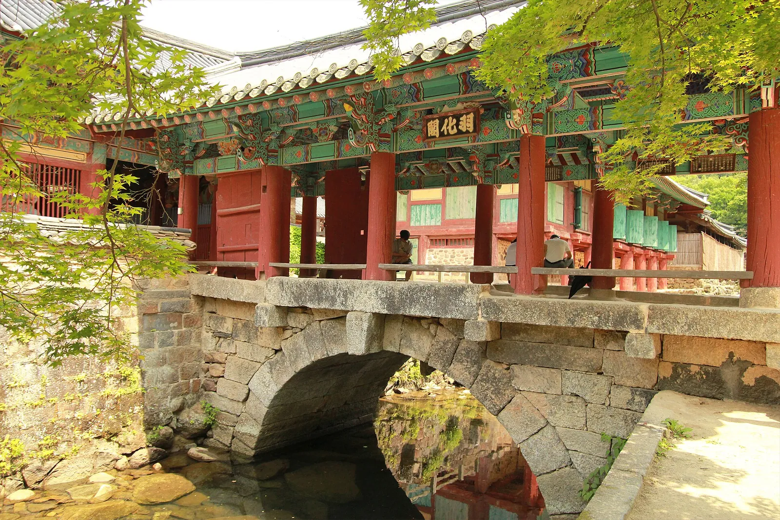 A stone arch bridge over a stream below a red-pillared pavilion at Songgwangsa temple