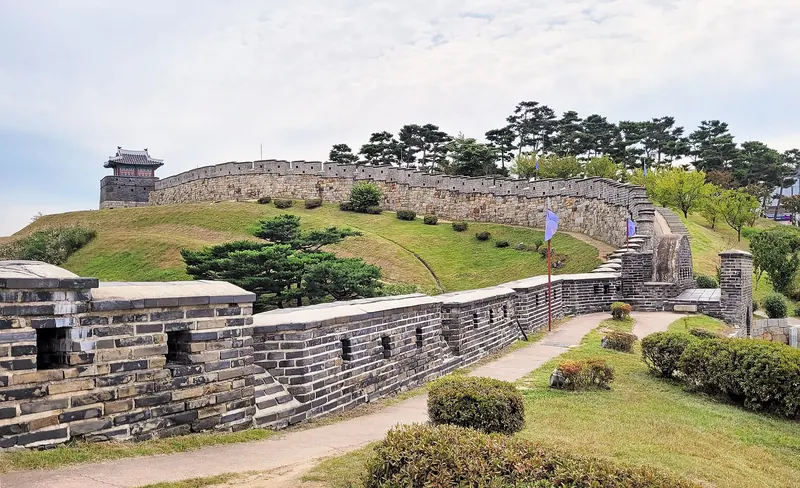 Stone wall of Hwaseong Fortress running up a green hillside to a small watchtower, Suwon