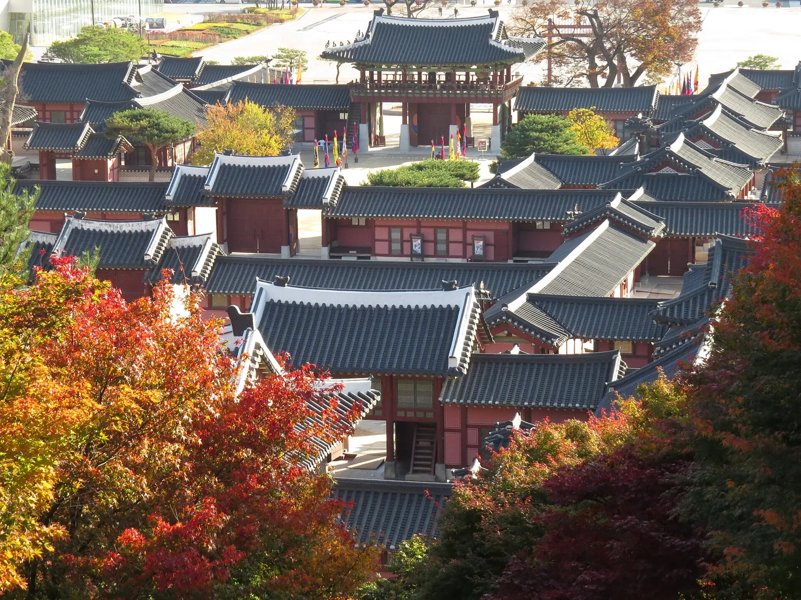 Tiled rooftops of the Hwaseong Haenggung palace seen from above among red and orange autumn trees