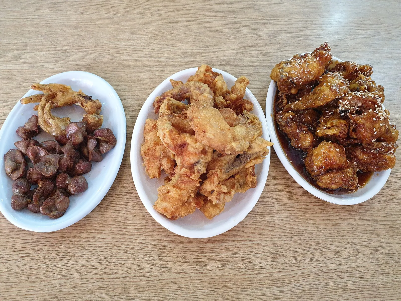 Three bowls from Suwon Chicken Street: fried gizzards, plain fried chicken and a darker glazed fried dish with sesame