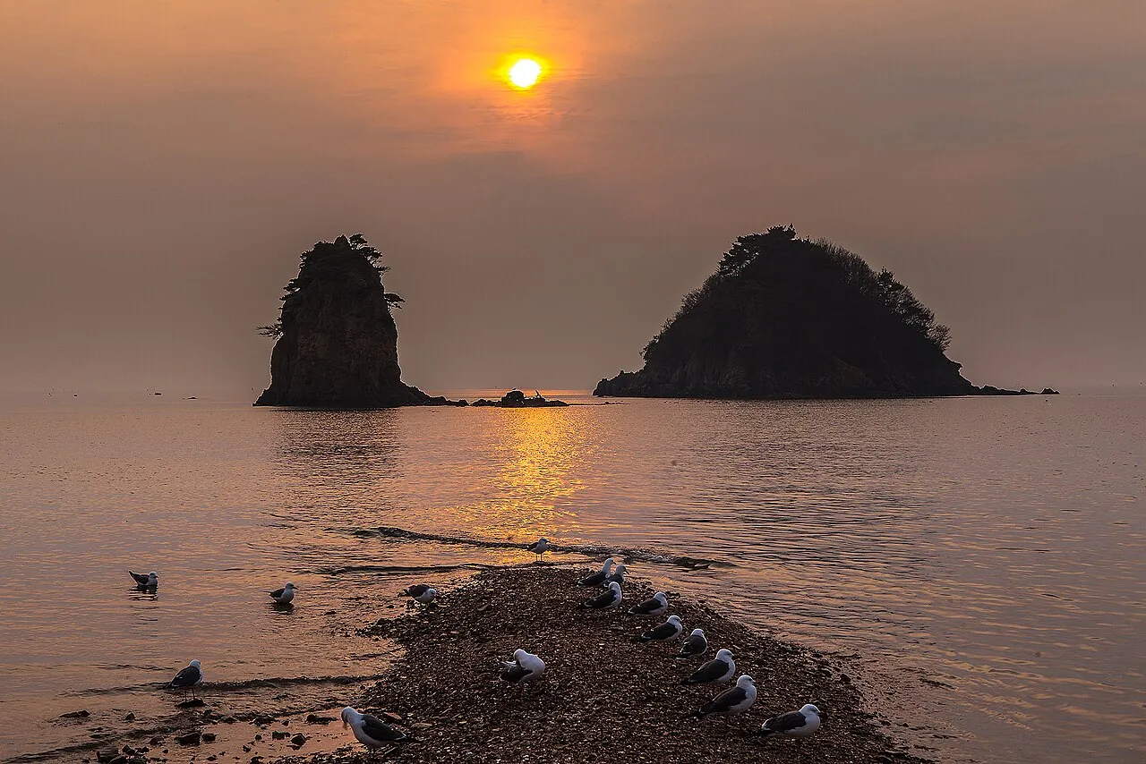 The sun setting behind the two rock islets of Halmibawi and Halabibawi off Kkotji Beach, with gulls on a sand spit