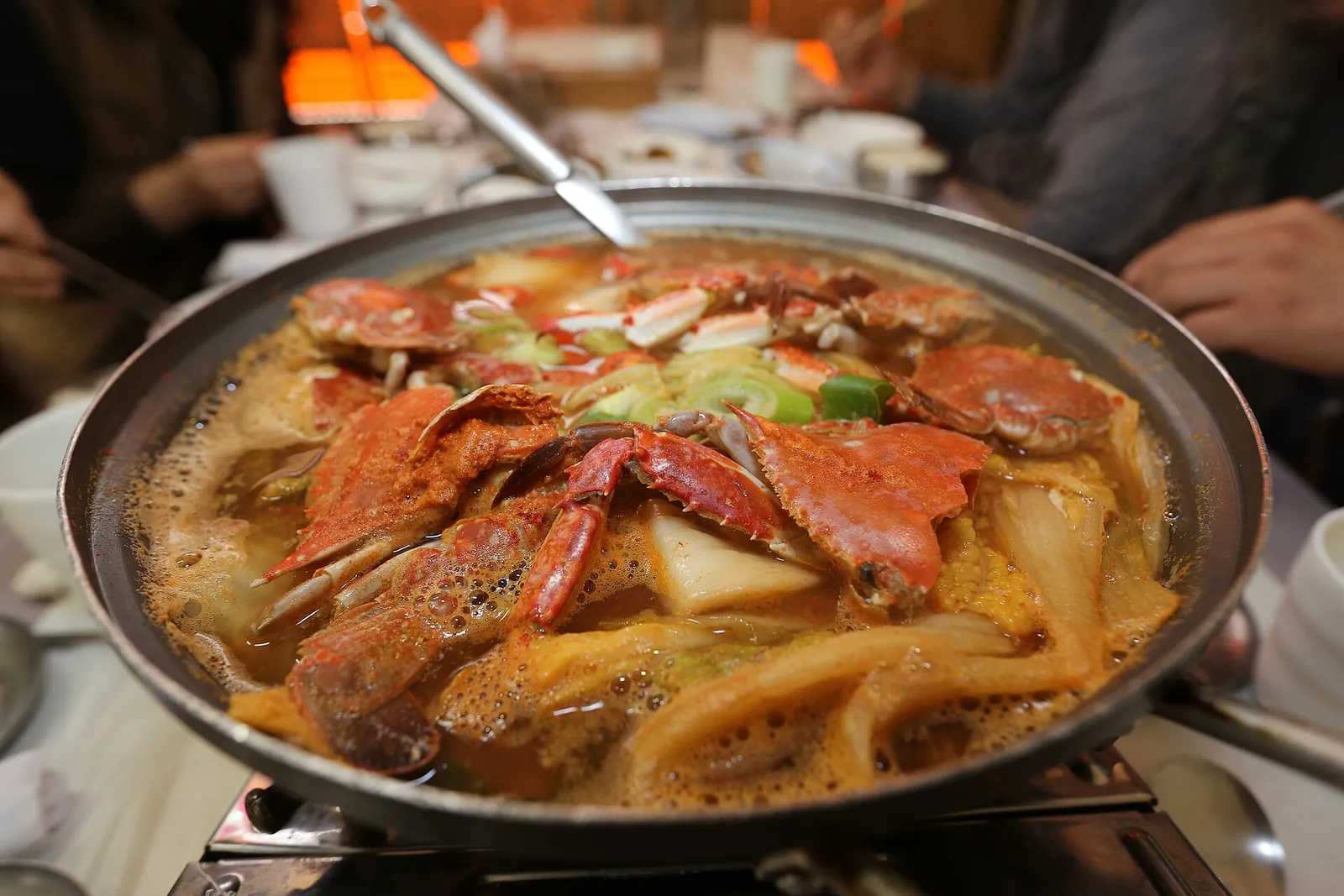 A pan of gegukji, blue crab stewed with kimchi and vegetables, on a table burner