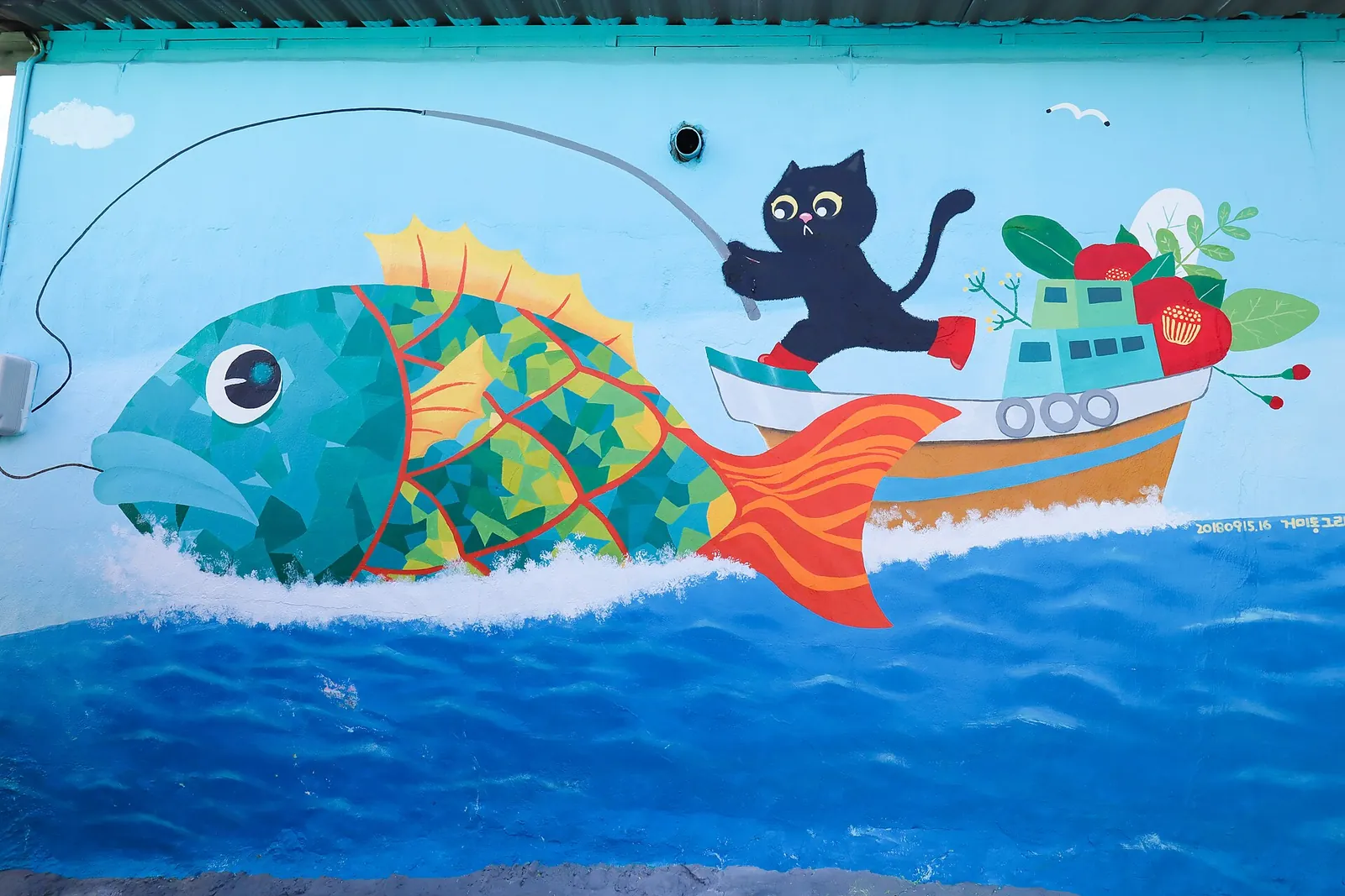 Mural of a large fish and a black cat fishing from a boat on a blue wall in Dongpirang Village