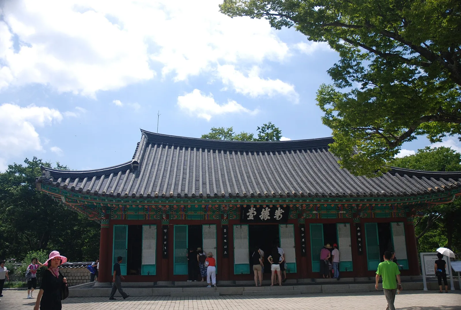 Jeseungdang, a single-storey hall with a tiled roof among trees on Hansando, with visitors in front