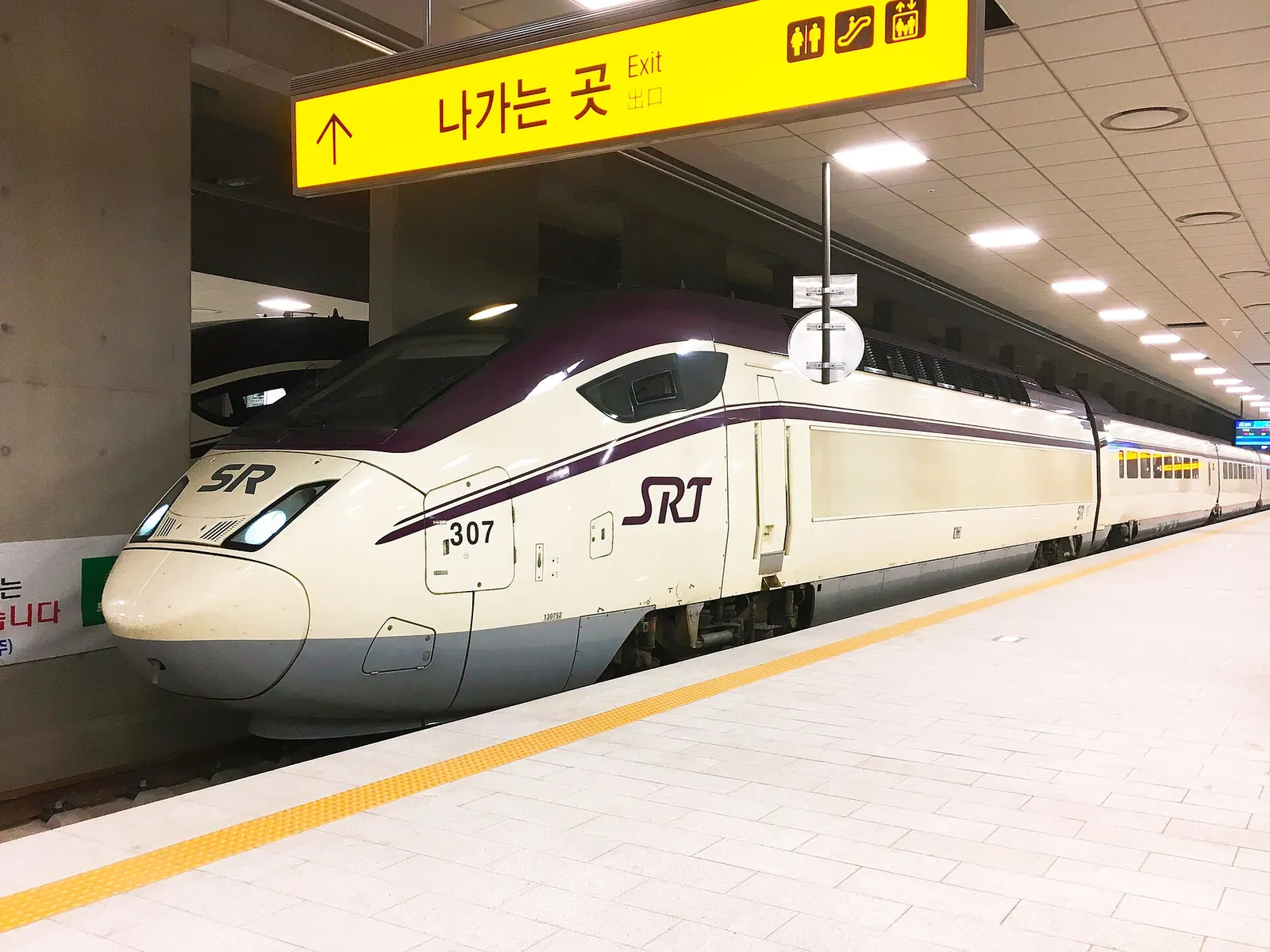 Purple-and-white SRT high-speed train at a platform in Suseo Station, Seoul, under a yellow exit sign