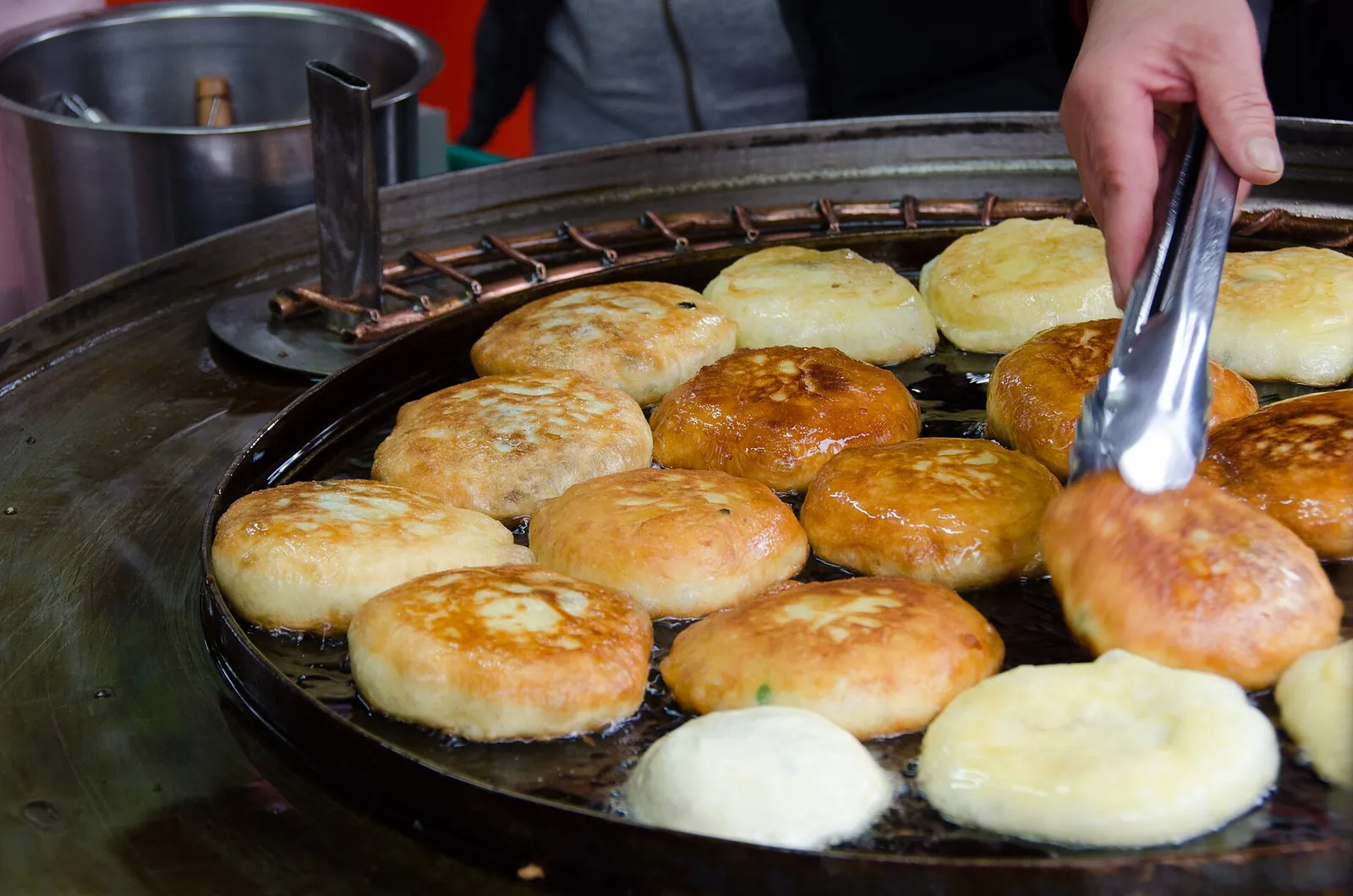 Hotteok pancakes frying on a round griddle, turned with tongs