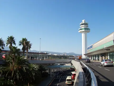 Kontroltårnet og terminalen på Jeju Internationale Lufthavn under en klar blå himmel, med palmer ved adgangsvejen