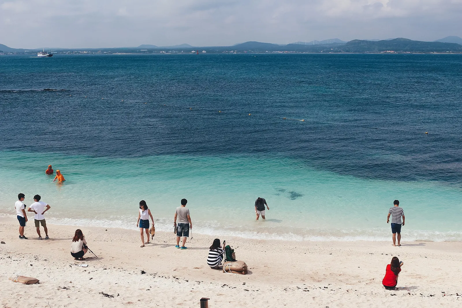 Visitors on the white beach of Seobin Baeksa on Udo, with turquoise shallows and deep blue sea beyond