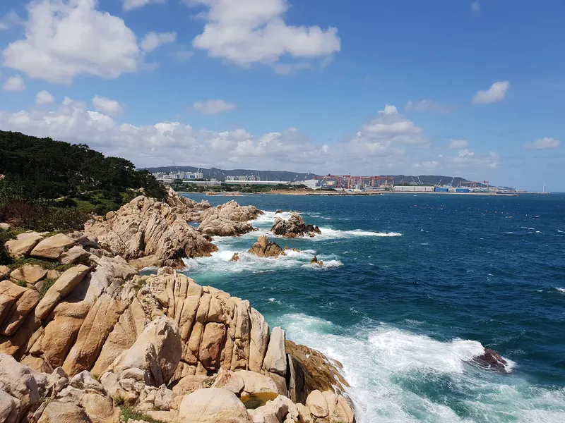 Granite rocks and blue sea at Daewangam Park on the Dong-gu coast of Ulsan, with buildings on the far shore