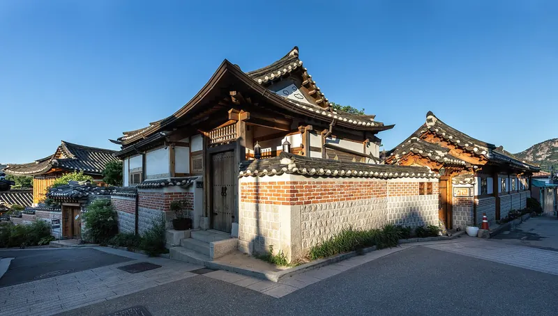 Traditional hanok houses with tiled roofs and stone walls under a blue sky in Bukchon Hanok Village, Seoul