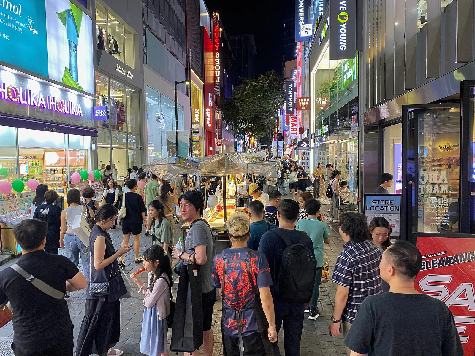 Crowds walking past street-food stalls and cosmetics shops in Myeongdong, Seoul, in the evening