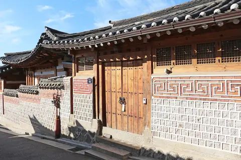 Et hanok-hus med tegltag, trædøre og en mønstret stenmur i hanok-landsbyen Bukchon i Seoul