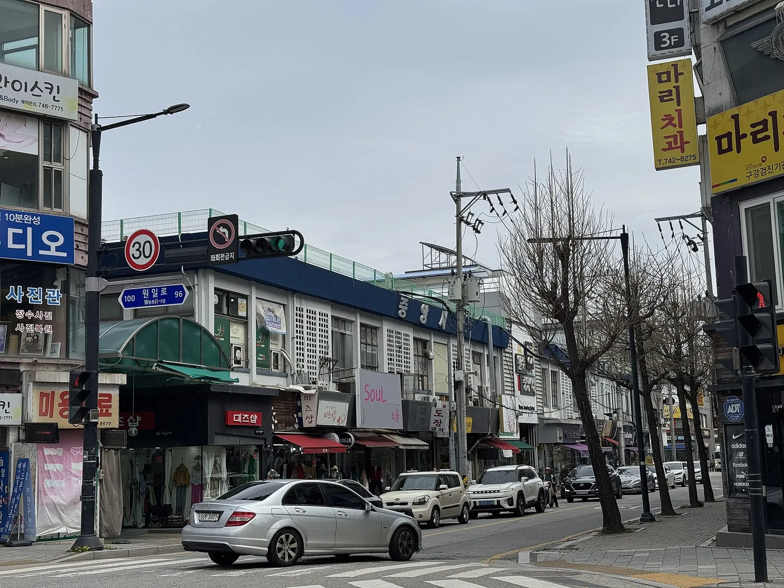 A street of low shop buildings with signs along the outside of Wonju Jungang Market on a grey spring day