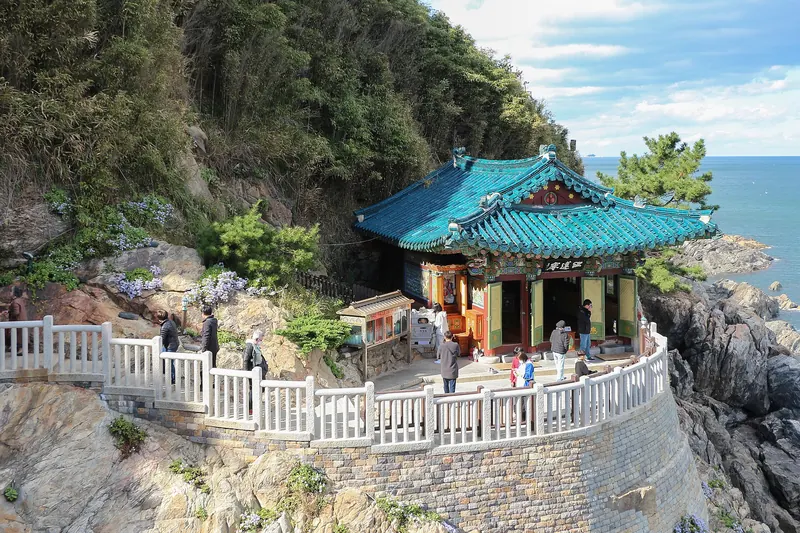 Hongnyeonam Hermitage with a blue-tiled roof on a rocky sea cliff at Naksansa, with the East Sea beyond