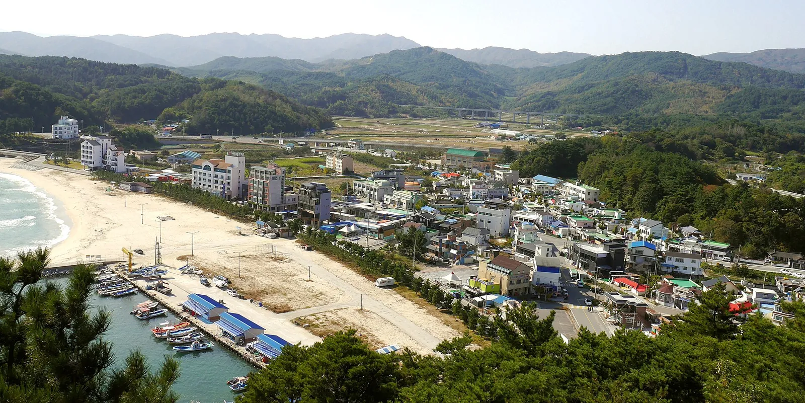 Ingu beach and harbour seen from above, with the village and green hills behind
