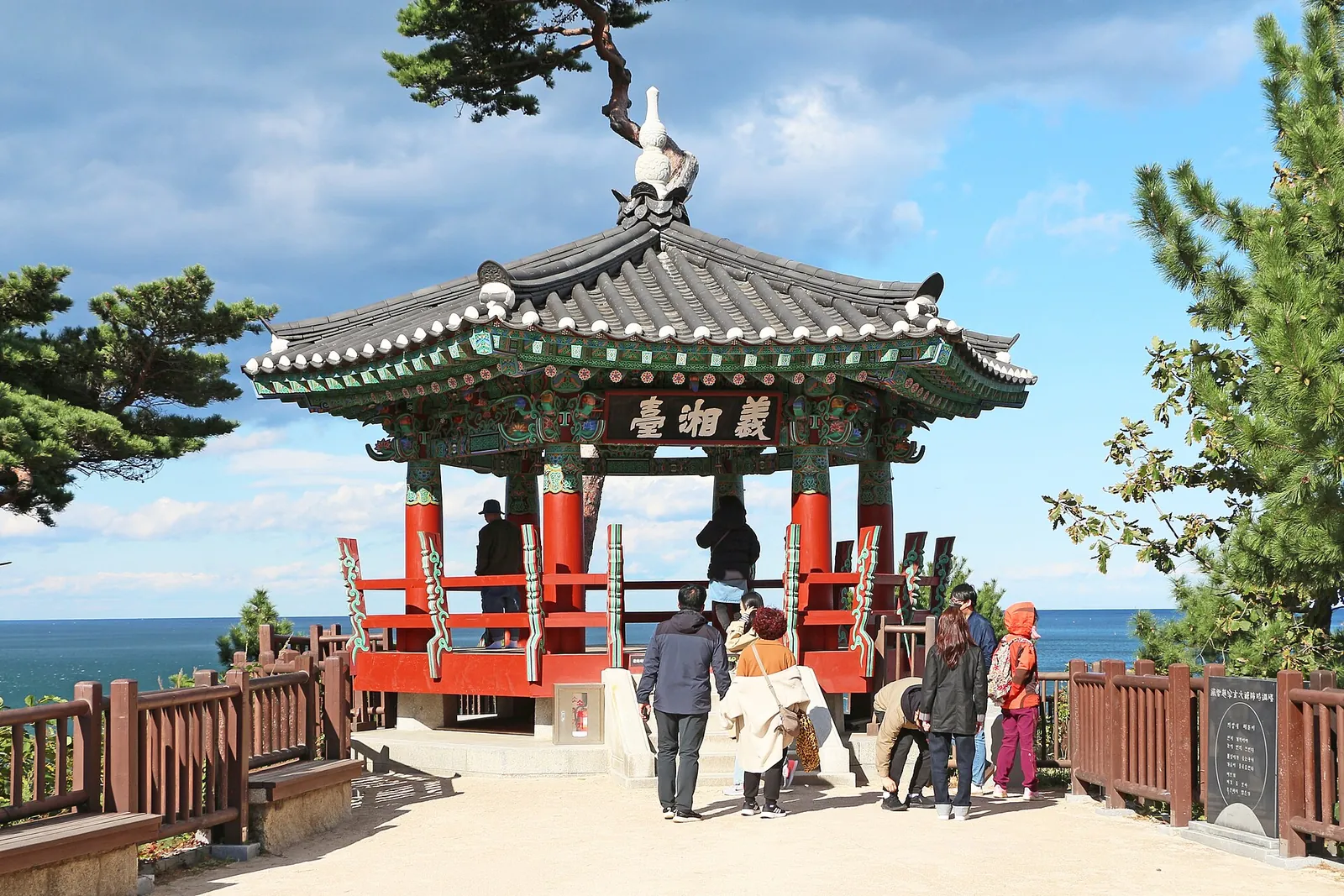 Uisangdae, a hexagonal painted pavilion on a pine-covered cliff above the sea, with visitors on the terrace
