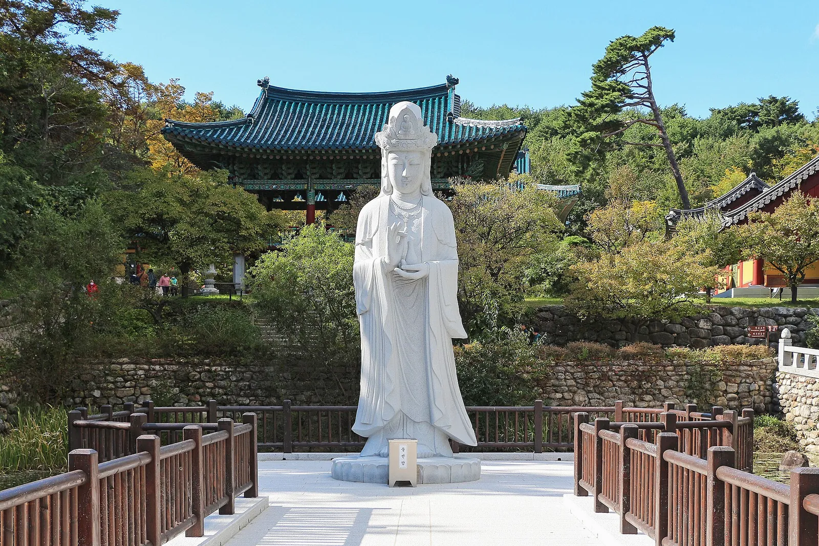 White stone statue of a bodhisattva on a terrace in front of temple halls and pine trees at Naksansa