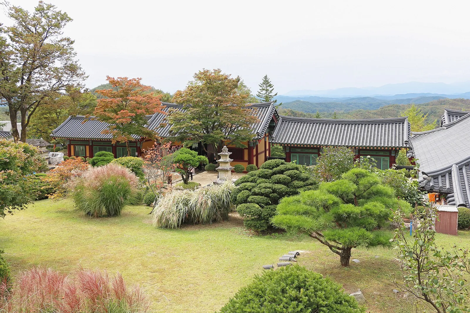 Autumn garden of clipped pines and grasses among tiled-roof halls at Buseoksa Temple, with mountain ridges behind