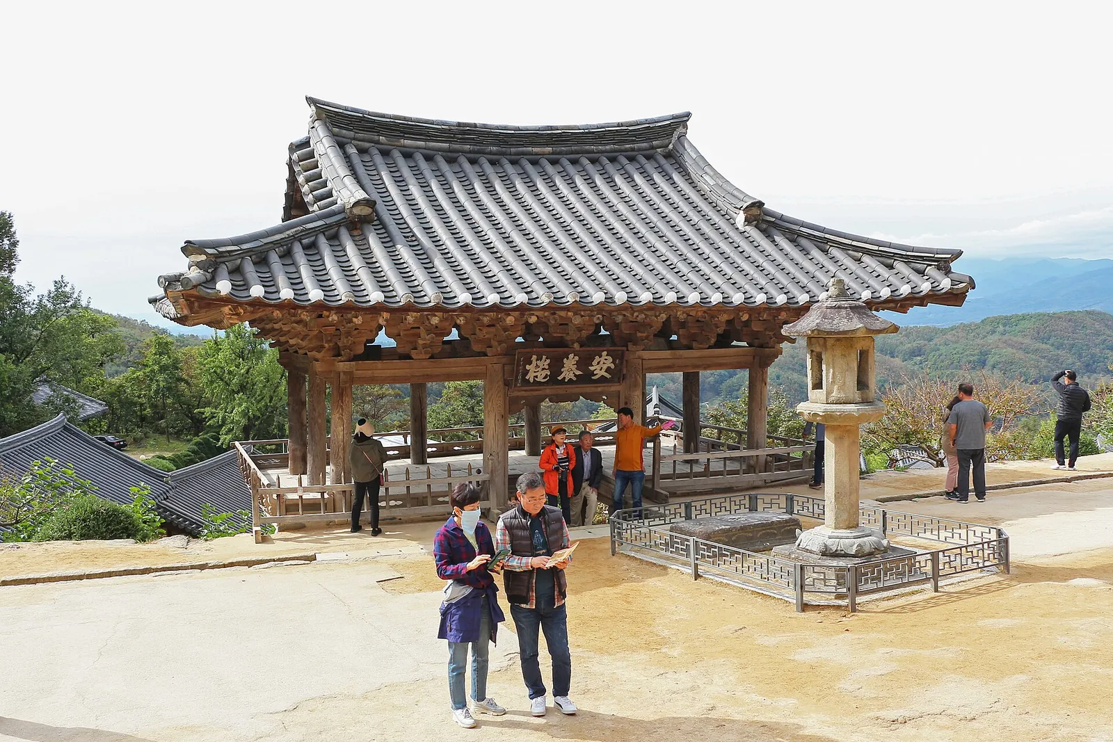 Visitors beside Anyangnu Pavilion and a stone lantern on a terrace at Buseoksa Temple, looking out over the mountains