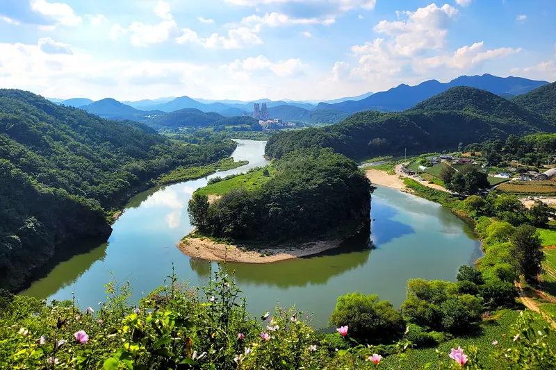 The Korean Peninsula Terrain in Yeongwol: a wooded headland shaped like the Korean Peninsula inside a green river bend, under a blue sky