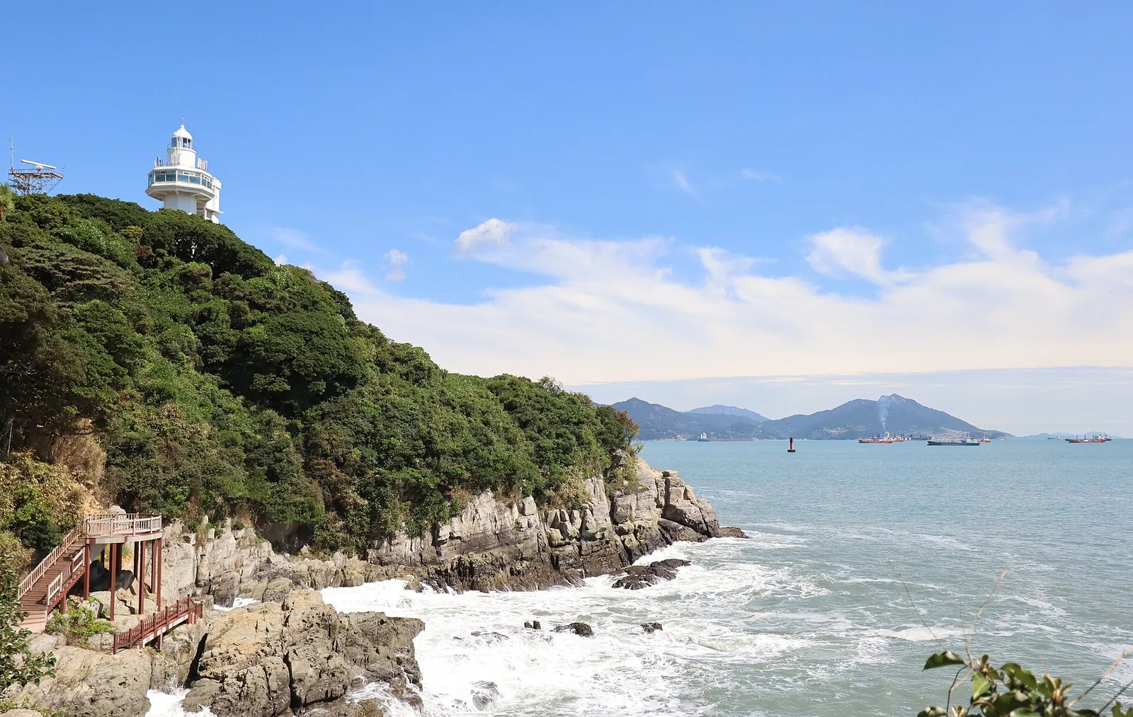 Rocky coastline of Odongdo Island with the white lighthouse above the camellia woods and the sea beyond