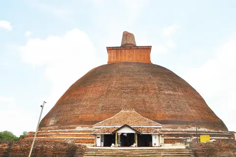 Die Backsteinkuppel der Jetavanaramaya-Stupa unter blauem Himmel, mit dem Eingangsportal am Sockel