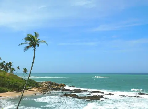 Bølger, der brydes mod klipper, og en sandet bugt under en blå himmel ved Mirissa, Sri Lanka
