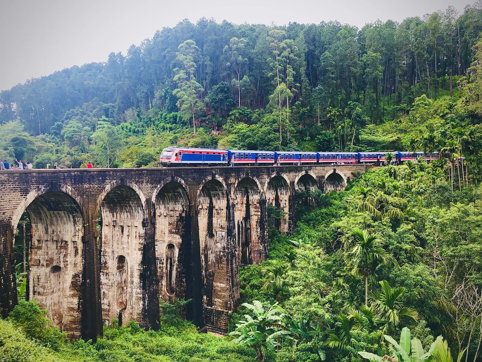 Un tren albastru de pasageri care trece peste Podul Nine Arch printre păduri, la Ella, Sri Lanka