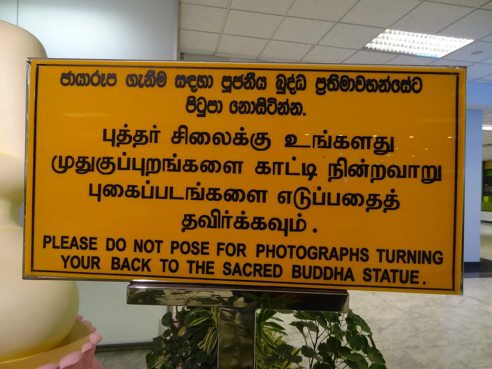 Un cartel bilingüe del aeropuerto internacional Bandaranaike que pide a los visitantes que no posen para fotografías de espaldas a la estatua de Buda