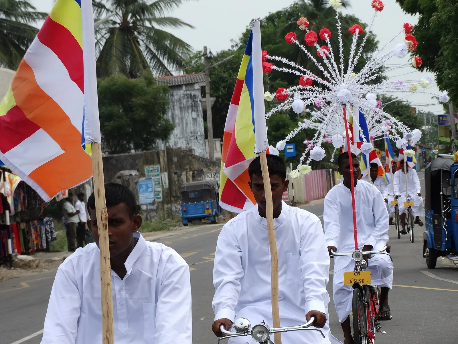 Muži v bílém jedou s buddhistickými vlajkami na kole po ulici v Jaffně během Vesak