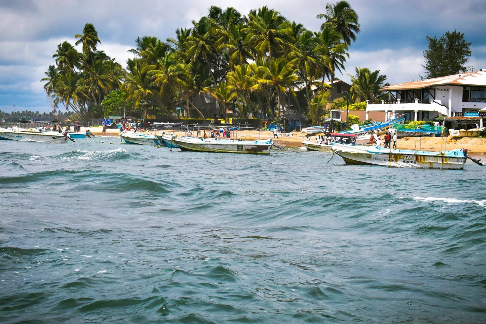Fischerboote auf bewegter See vor einem palmengesäumten Strand bei Hikkaduwa, Sri Lanka