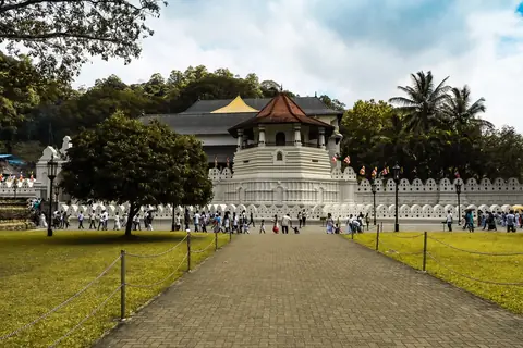 Der Zahntempel in Kandy, über einen Rasen hinweg gesehen, mit dem weißen achteckigen Pavillon und Palmen