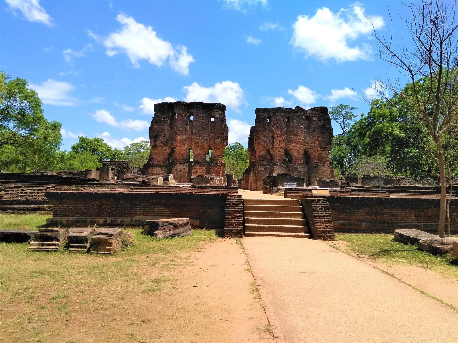 Dos altos muros de ladrillo del palacio real de Parakramabahu vistos al otro lado de un patio de hierba en Polonnaruwa