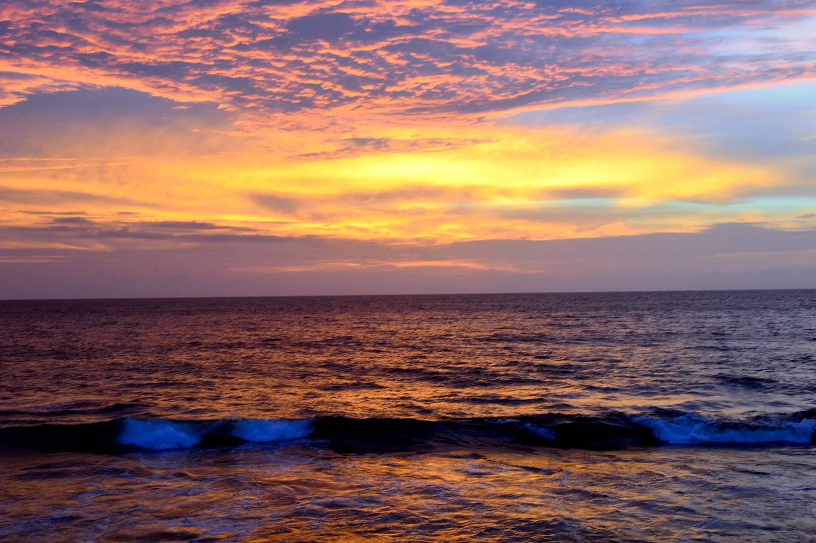 Bølger og en orange og lyserød solnedgangshimmel over havet ved Galle Face i Colombo