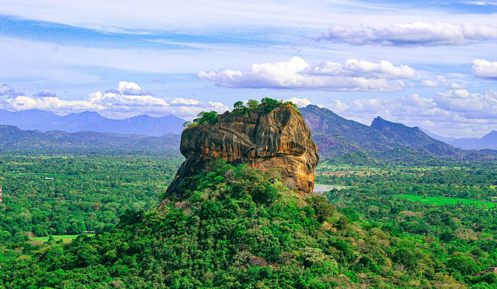 Sigiriya rock rising above green forest under a blue sky